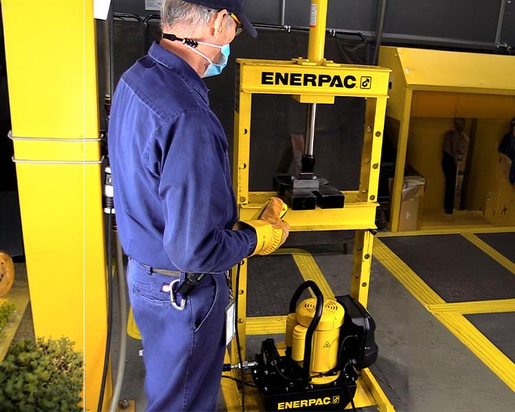 A construction worker wearing a hard hat, safety vest, and tool belt stands confidently next to a yellow featherlite ladder in a bright indoor setting.