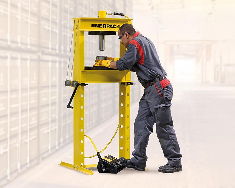 A construction worker wearing a hard hat, safety vest, and tool belt stands confidently next to a yellow featherlite ladder in a bright indoor setting.