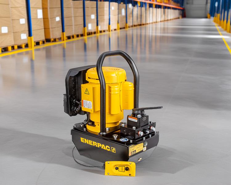 A construction worker wearing a hard hat, safety vest, and tool belt stands confidently next to a yellow featherlite ladder in a bright indoor setting.